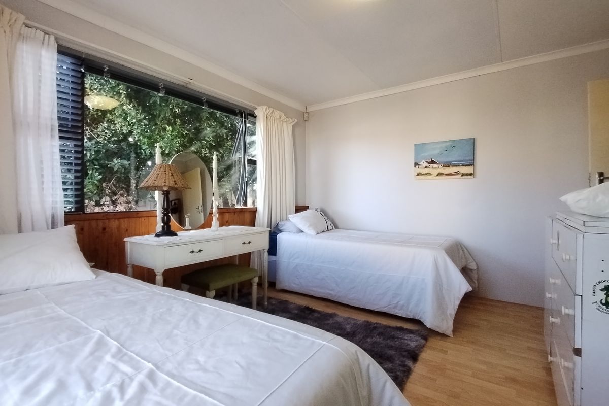 A bedroom featuring laminate flooring, wooden wall paneling, and a large window providing natural light and garden views.