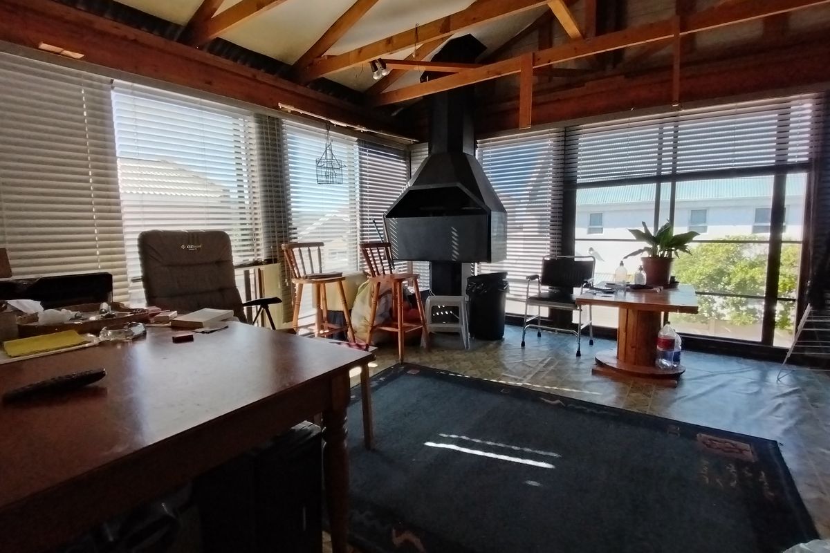 Spacious living area featuring exposed timber rafters, a central freestanding metal fireplace, and large windows with venetian blinds providing ample natural light.