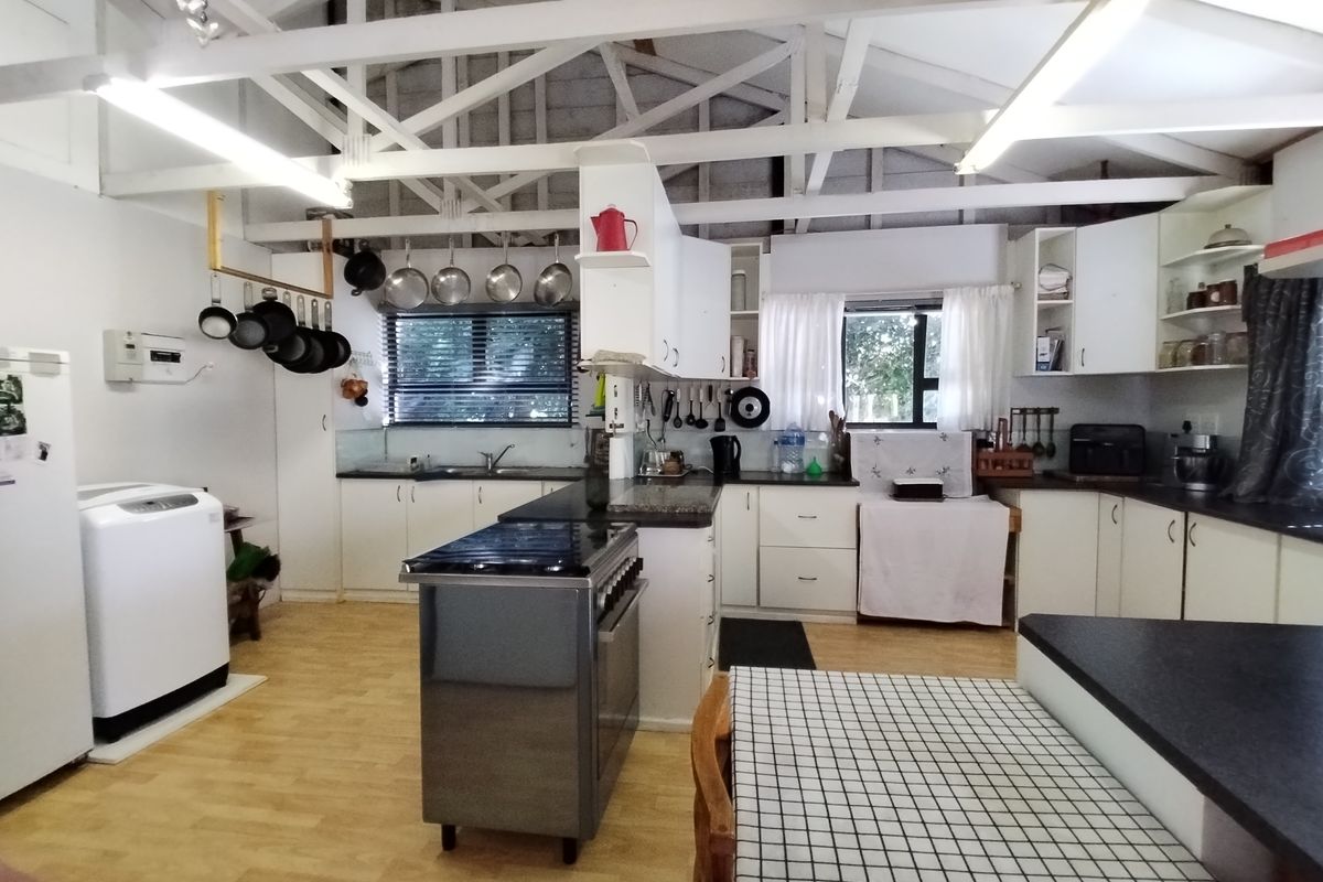 Spacious kitchen featuring exposed timber roof trusses, ample built-in cabinetry, laminate countertops, and a functional layout with a central freestanding stove.