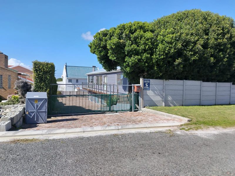 Front view of the property featuring a metal driveway gate, brick paved entrance, and a raised wooden deck attached to the main structure.