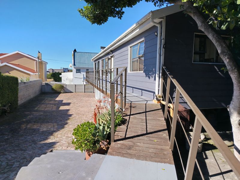 Rear exterior view featuring a raised timber deck with metal railings, paved driveway, and grey timber-clad siding.