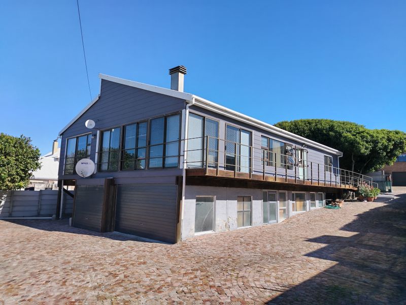 Rear view of a multi-level house featuring a raised timber deck, large windows, and a paved driveway area.