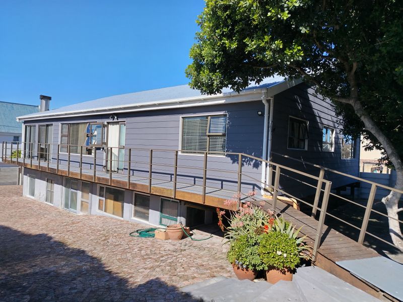 Rear view of the property featuring a raised timber deck with a ramp, metal balustrades, and cobblestone paving in the garden area.