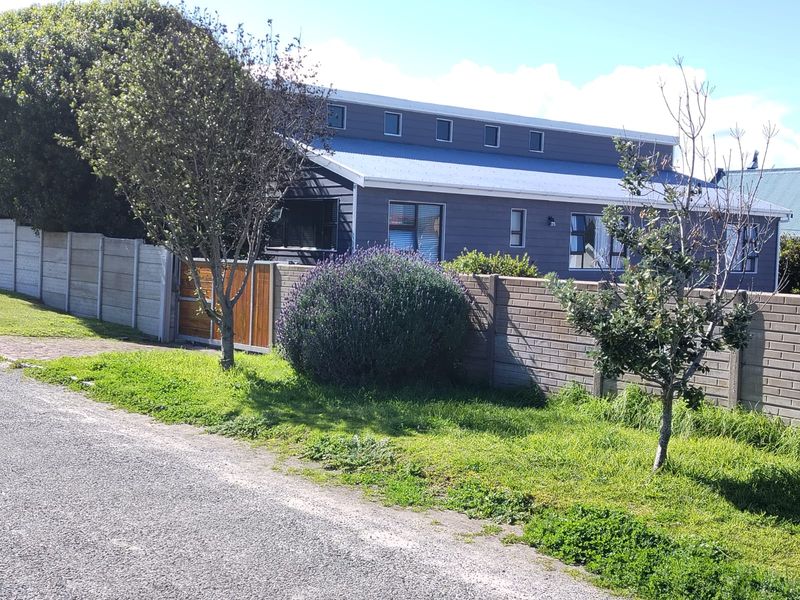 Front view of a modern house featuring dark grey cladding, a metal roof, and secure brick and concrete boundary walls with a timber gate.