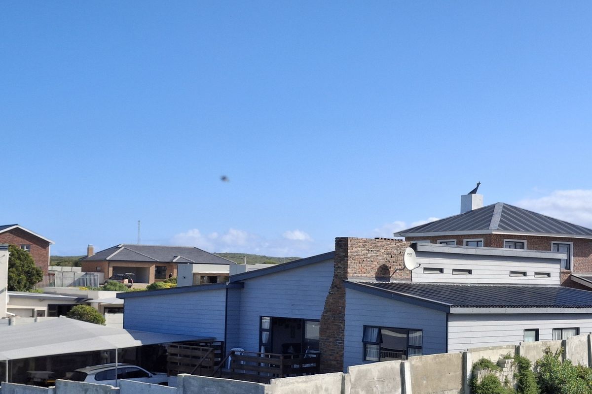 An elevated view of the rear exterior of the property, showcasing the metal roofing, brick chimney, and surrounding residential neighbourhood.