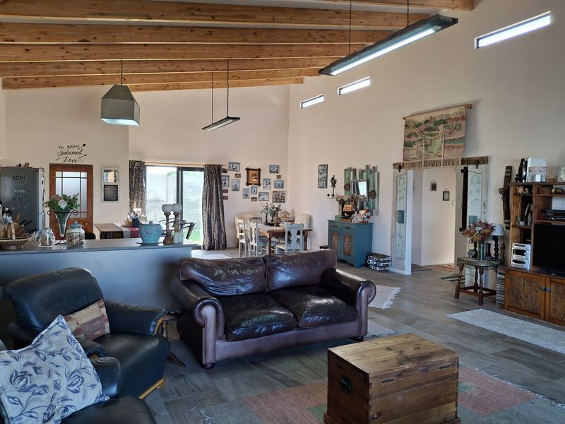 Spacious open-plan living area featuring exposed timber ceiling beams, tiled flooring, and abundant natural light from clerestory windows and sliding glass doors.
