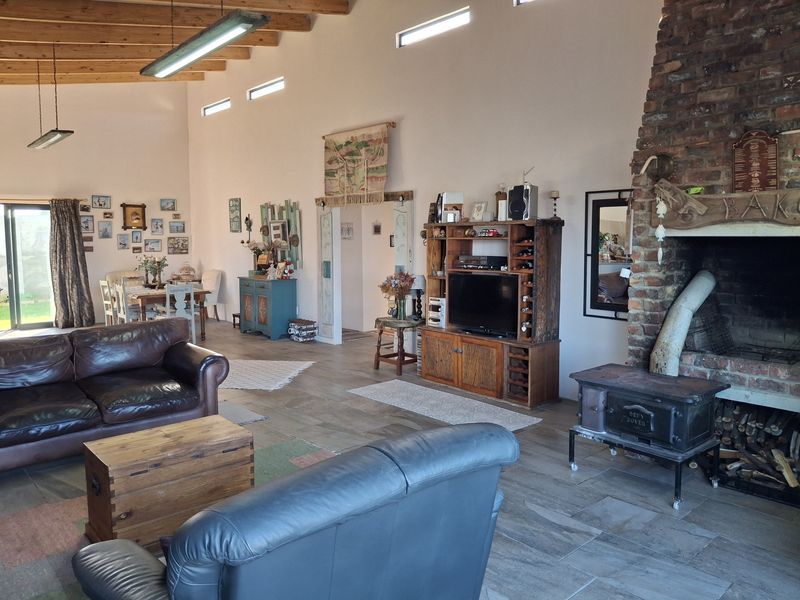 Spacious open-plan living area featuring high exposed timber beam ceilings, a large brick fireplace with a wood-burning stove, and tiled flooring throughout.