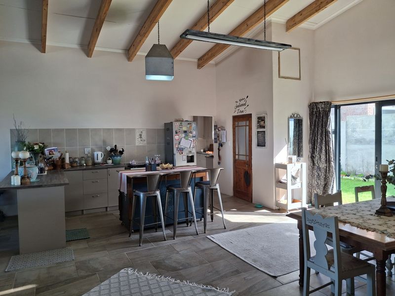 Spacious open-plan kitchen and dining area featuring exposed timber ceiling beams, tiled flooring, and direct access to the garden through sliding glass doors.