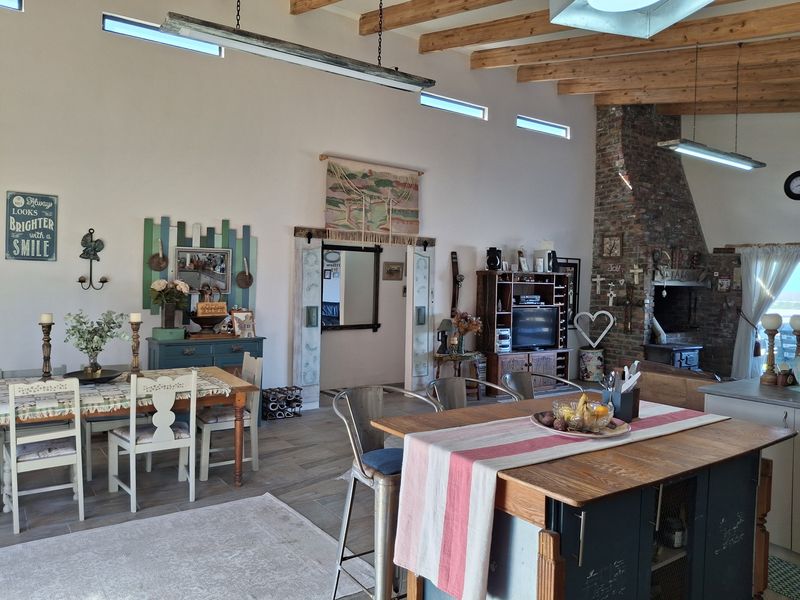 Spacious open-plan living and dining area featuring exposed timber beams, a prominent brick fireplace, and modern clerestory windows providing natural light.