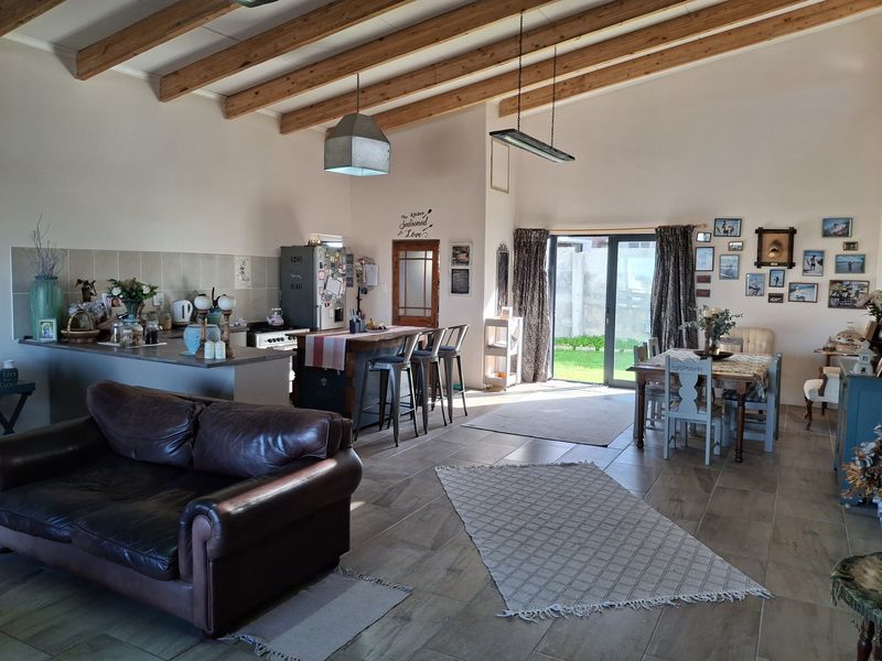 Spacious open-plan living and kitchen area featuring exposed timber ceiling beams, tiled flooring, and direct access to the garden through sliding glass doors.