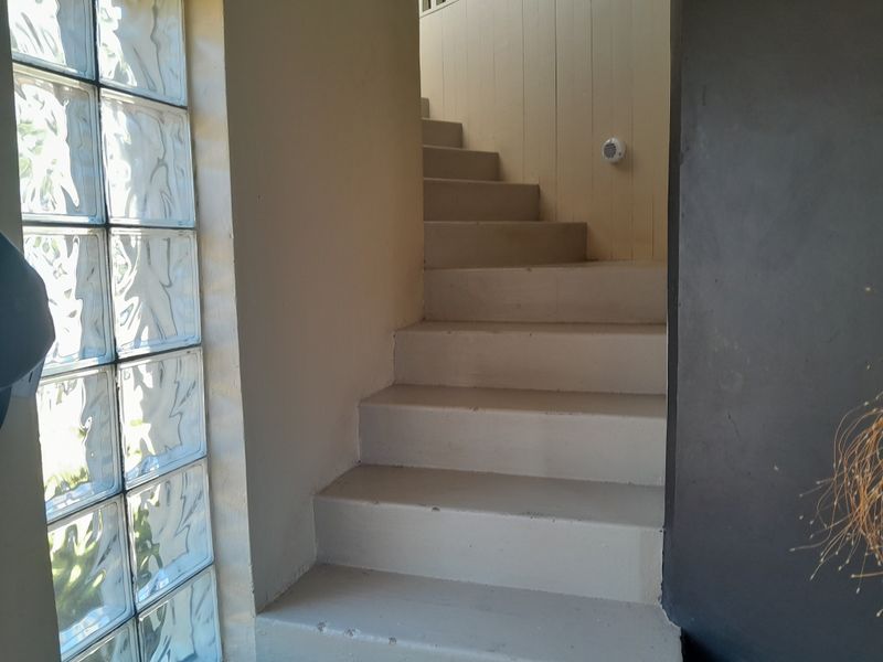 A functional interior staircase featuring painted concrete steps and a decorative glass block window providing natural light to the hallway area.