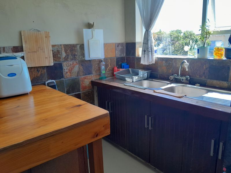A functional kitchen area featuring a double bowl stainless steel sink, slate tile splashback, and wooden cabinetry with a matching wooden countertop.