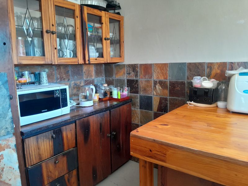 Kitchen area featuring rustic wooden cabinetry, a slate tile backsplash, and a wooden countertop, offering a dated aesthetic with potential for modernization.