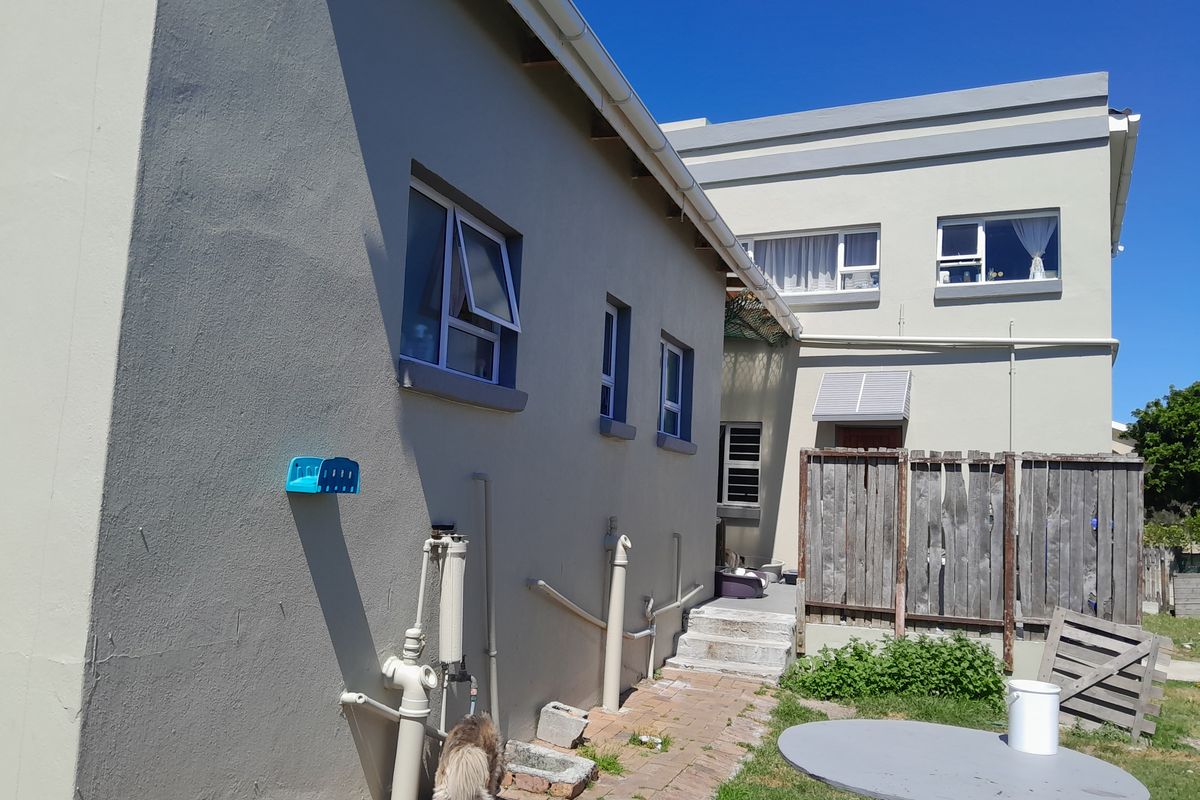 Rear exterior view of the property showing paved walkway, external plumbing fixtures, and timber fencing along the side of the building.