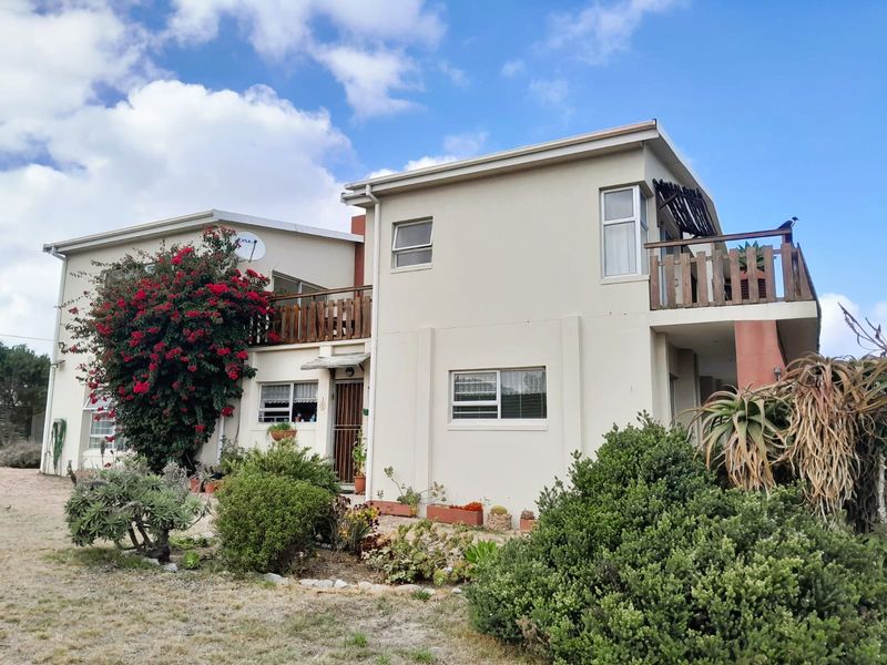 A two-story residential house featuring a neutral facade, upper-level balconies with wooden railings, and established garden landscaping.