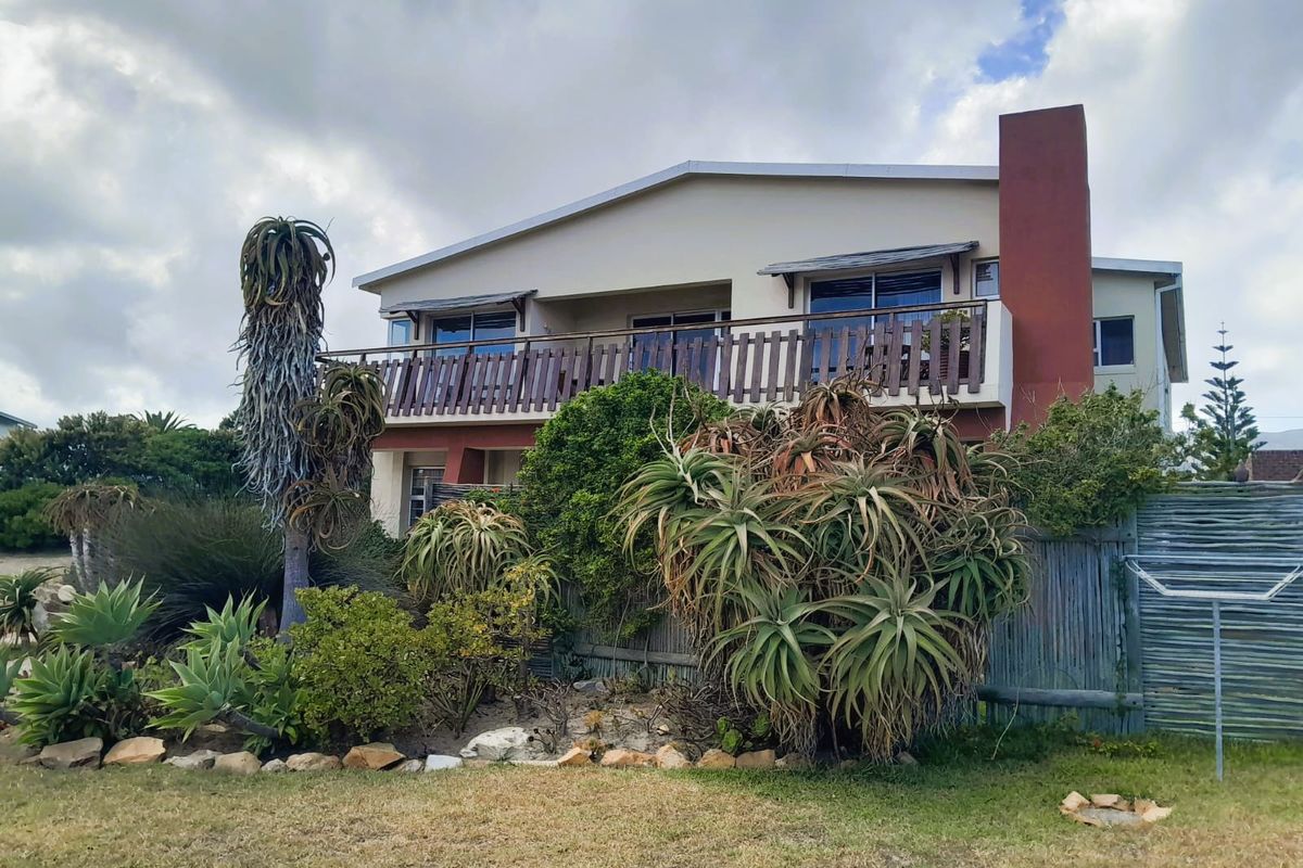 Rear view of a two-story house featuring a balcony with timber balustrade, a prominent chimney, and established garden landscaping.