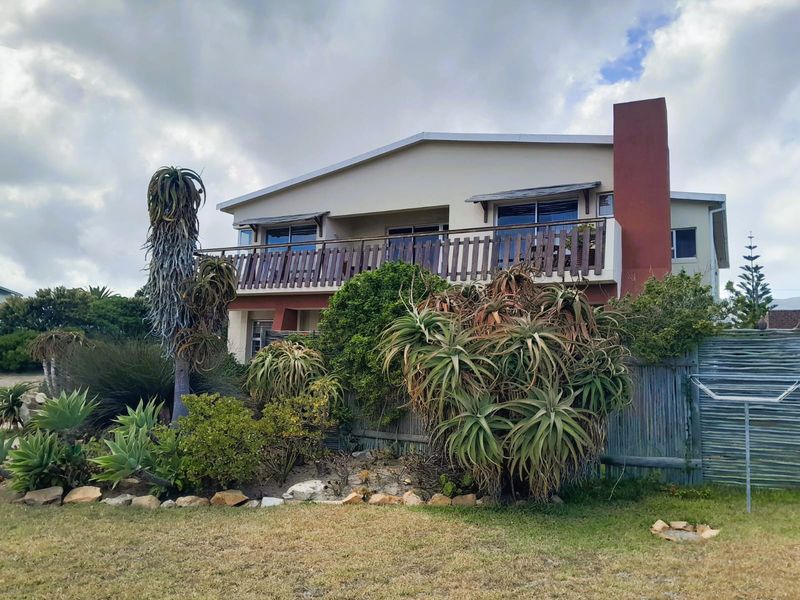 Rear view of a two-story house featuring a balcony with timber balustrade, a prominent chimney, and established garden landscaping.