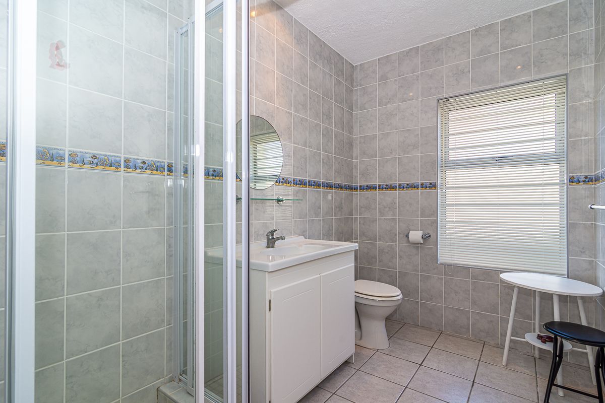 A functional bathroom featuring a shower enclosure, vanity basin, and toilet, finished with neutral wall and floor tiling.