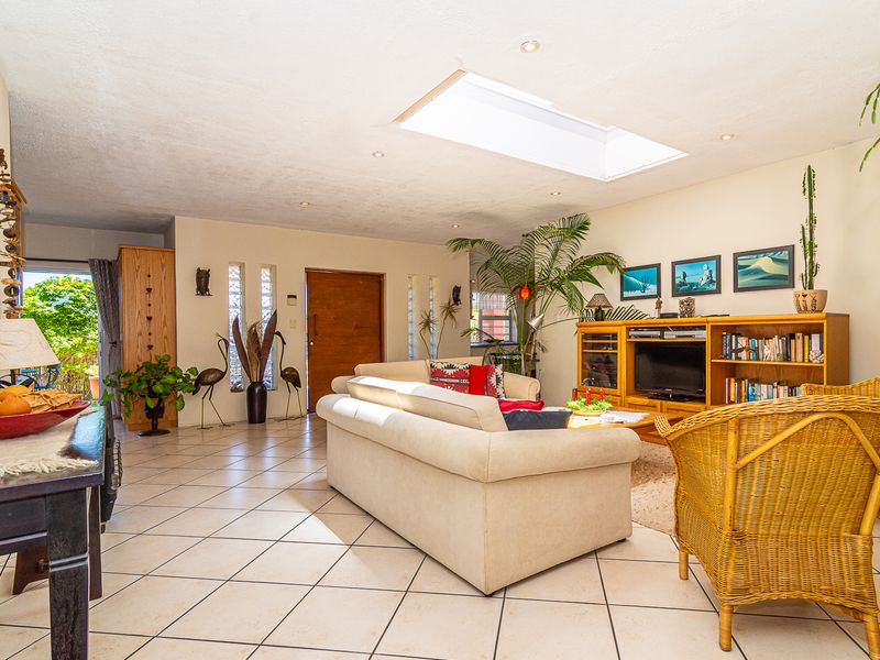 Spacious living room featuring ceramic floor tiles, a large skylight providing natural light, and vertical glass block accents near the solid wood entrance door.