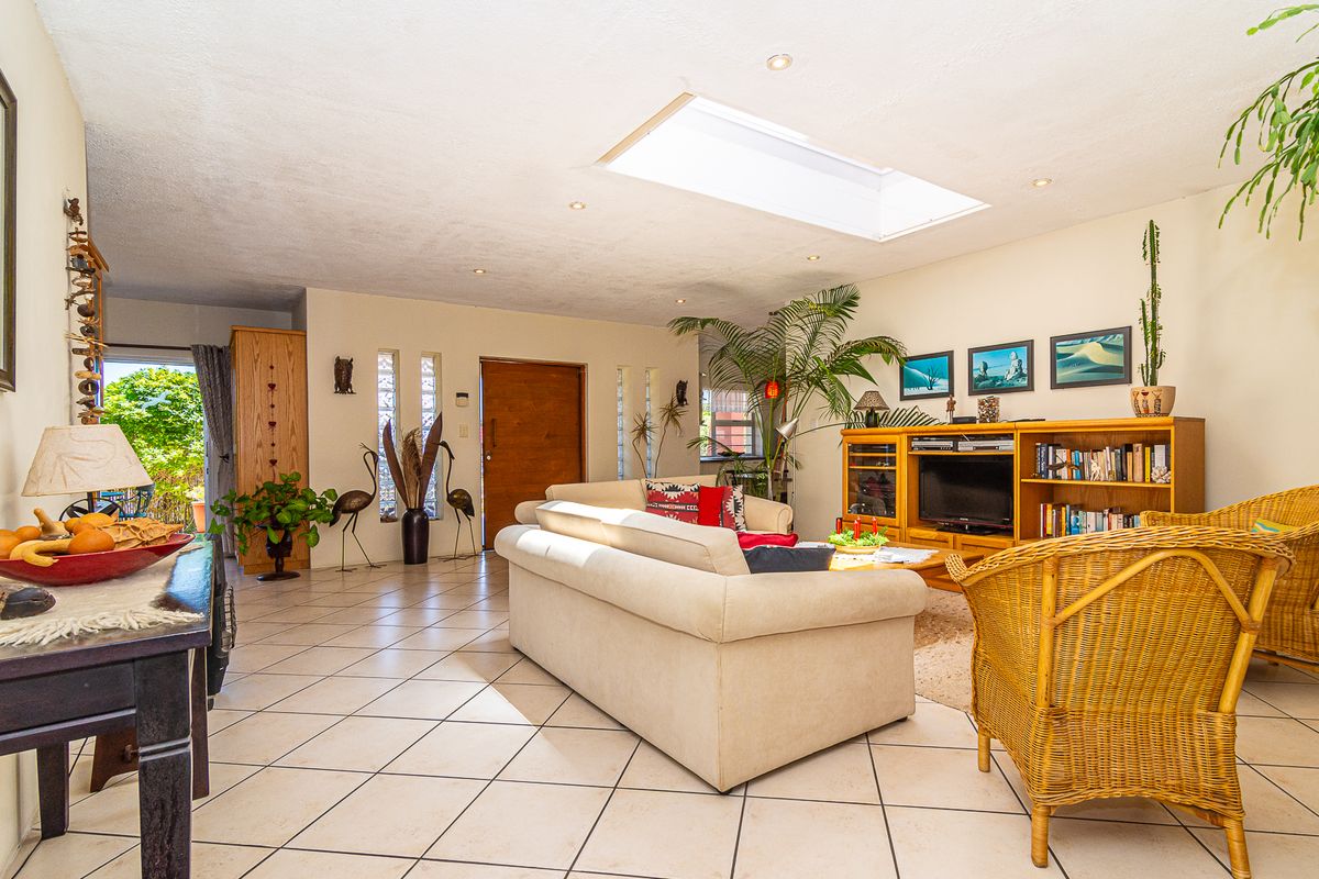 Spacious living room featuring ceramic floor tiles, a large skylight providing natural light, and vertical glass block accents near the solid wood entrance door.