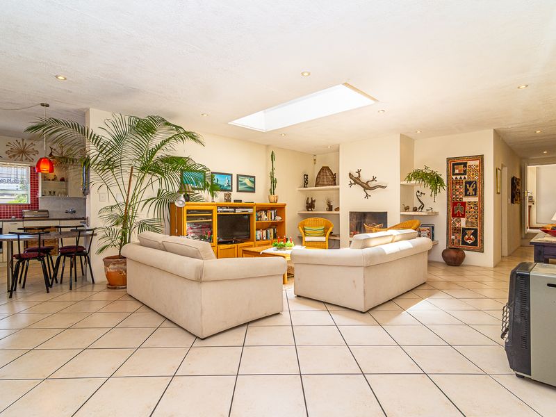 Spacious open-plan living area featuring a central skylight, tiled flooring, and an integrated fireplace, seamlessly flowing into a functional kitchen space.