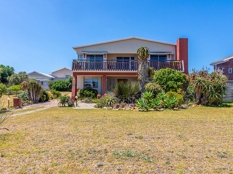 A two-story residential house featuring a front balcony with a wooden balustrade, a chimney, and a well-established landscaped garden with a paved walkway.