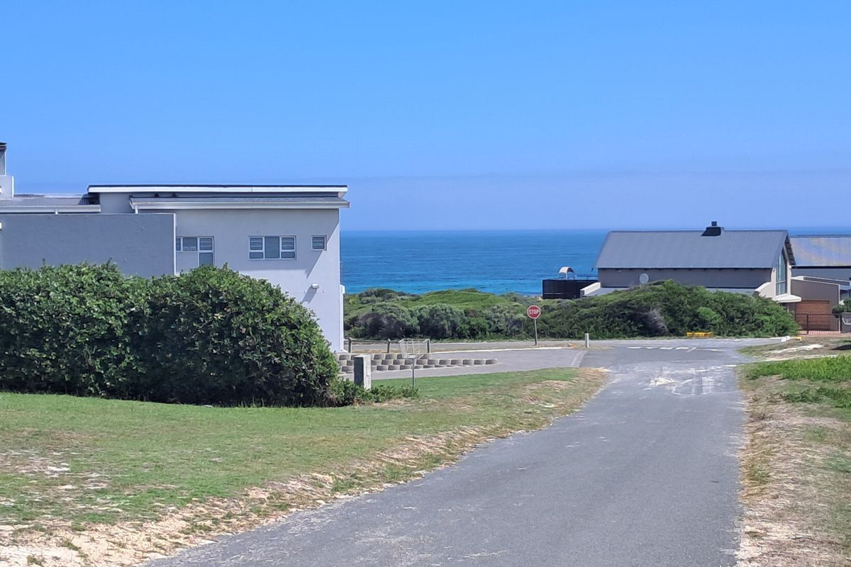 A scenic view of the coastal landscape featuring a paved road leading towards the ocean and surrounding residential properties.