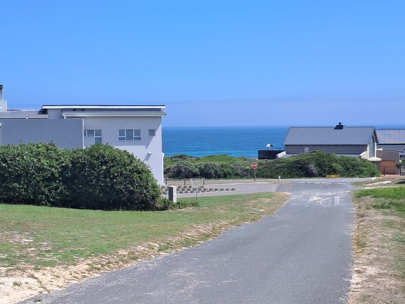 A scenic view of the coastal landscape featuring a paved road leading towards the ocean and surrounding residential properties.