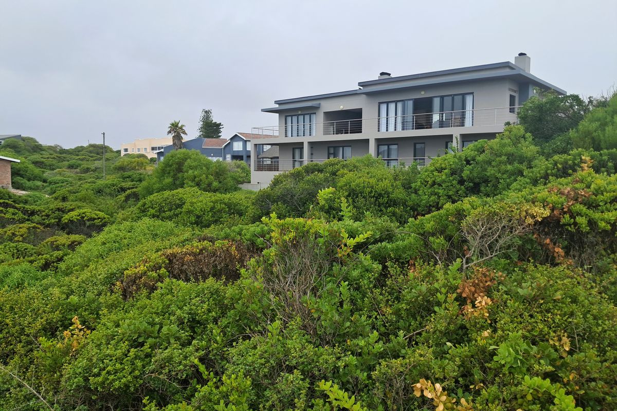 A view of the rear elevation of a multi-story residential property featuring balconies and sliding doors, surrounded by dense coastal vegetation.