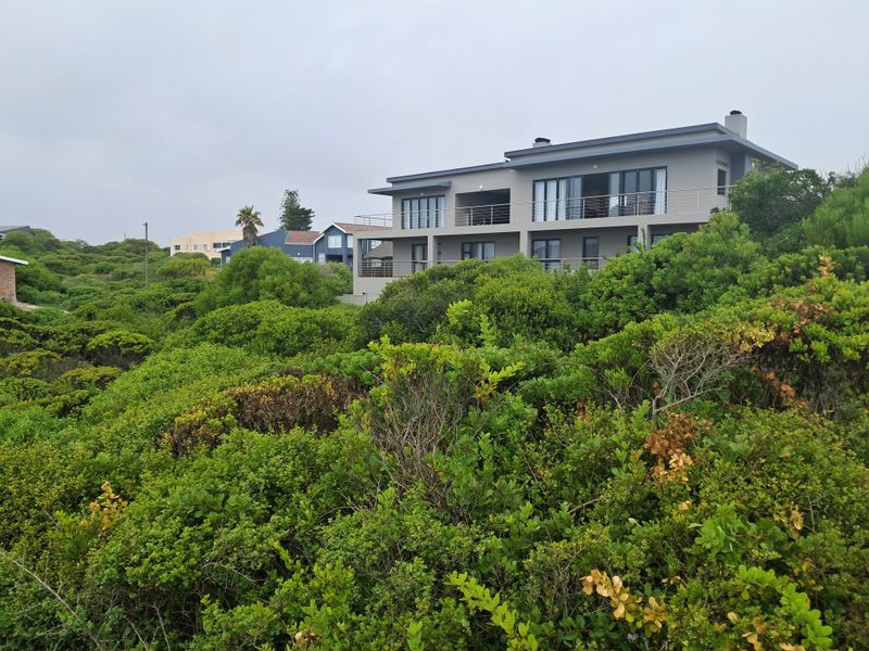 A view of the rear elevation of a multi-story residential property featuring balconies and sliding doors, surrounded by dense coastal vegetation.