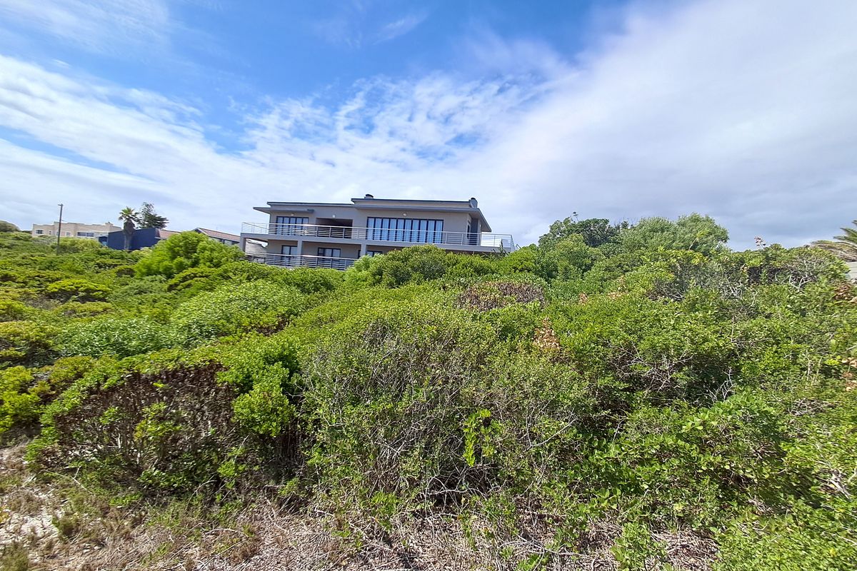 A view of a residential property set behind dense, natural coastal vegetation and fynbos, showcasing the building's exterior facade and balconies.
