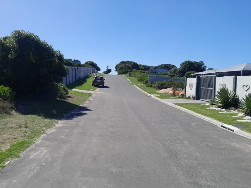 A view of the residential street approach, featuring paved road access and established boundary walls in a quiet neighborhood setting.