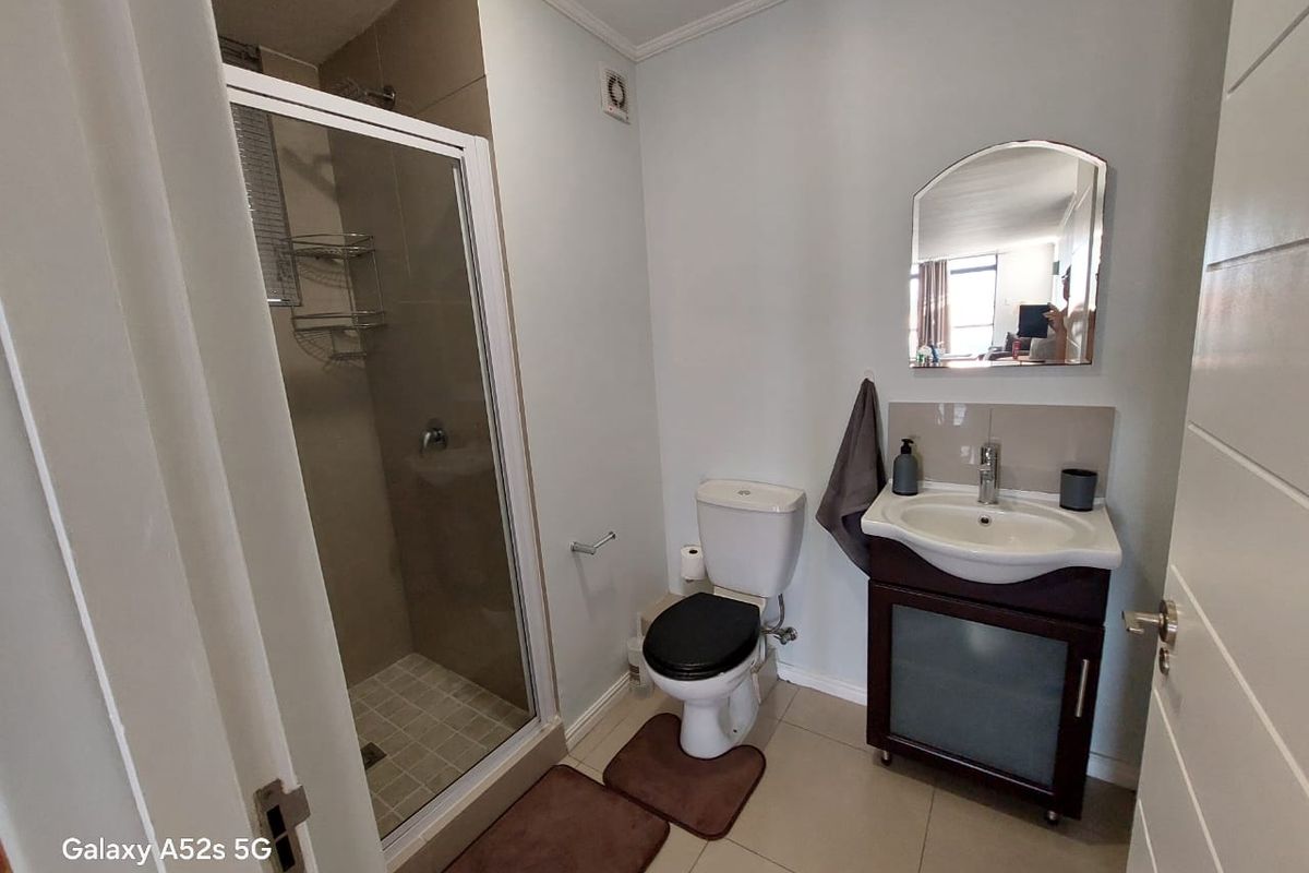 A functional bathroom featuring a glass-enclosed shower, a vanity unit with a basin, and a standard toilet, finished with neutral floor tiles.