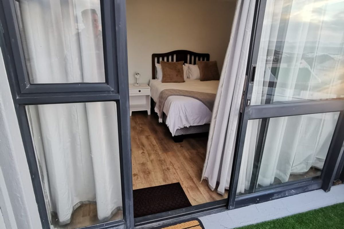 A bedroom with laminate flooring and sliding glass doors providing access to an outdoor patio area.