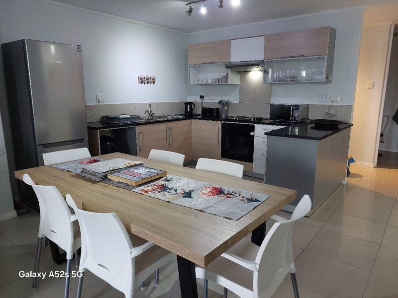 Open-plan kitchen and dining area featuring modern cabinetry, granite countertops, built-in oven, hob, and tiled flooring.
