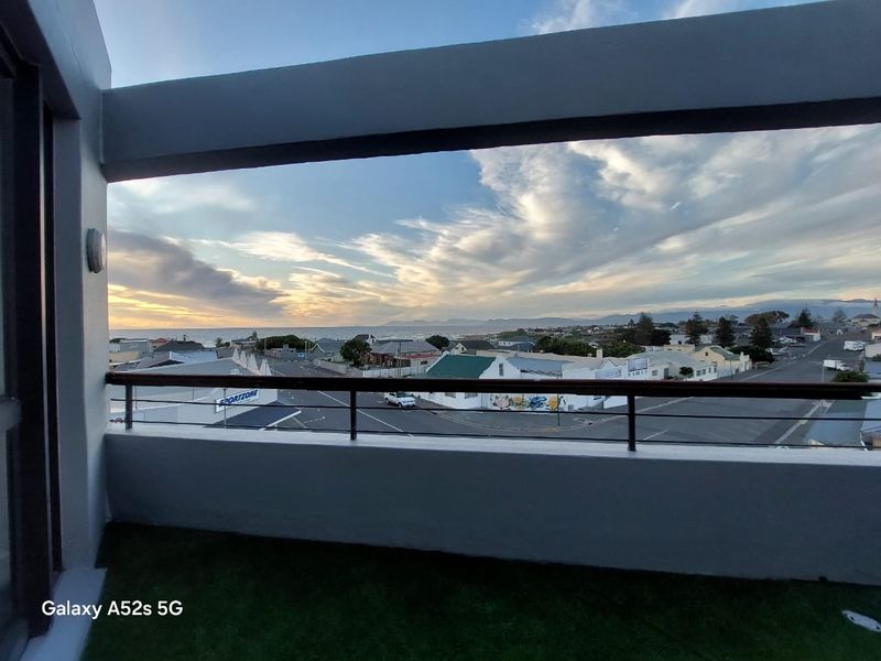 A balcony with a metal railing and concrete balustrade, offering expansive coastal and neighbourhood views.