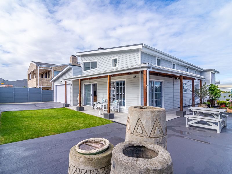 Rear view of the property featuring a covered timber pergola, paved patio area, well-maintained lawn, and modern light-colored cladding.