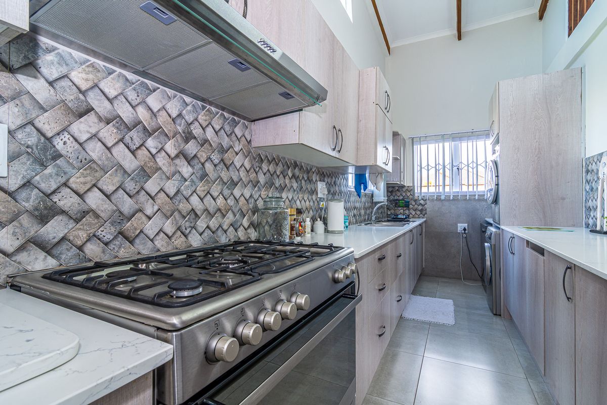 Modern kitchen featuring light wood cabinetry, stone countertops, a gas stove with extractor fan, and a decorative tiled backsplash.