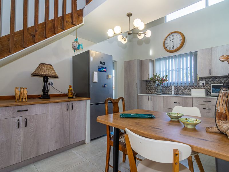 Open-plan kitchen and dining area featuring modern wood-look cabinetry, tiled backsplash, and a wooden staircase, creating a functional and cohesive living space.