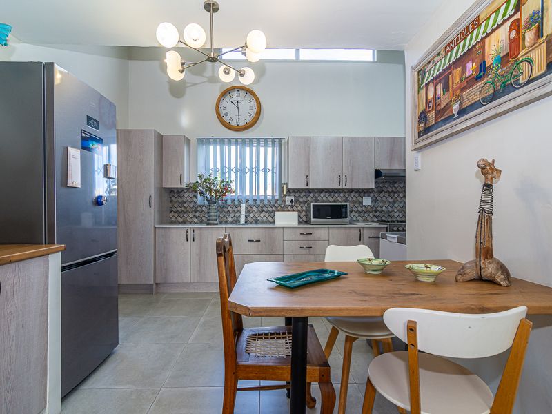 Open-plan kitchen and dining area featuring light wood-finish cabinetry, a decorative tiled backsplash, tiled flooring, and a modern chandelier.