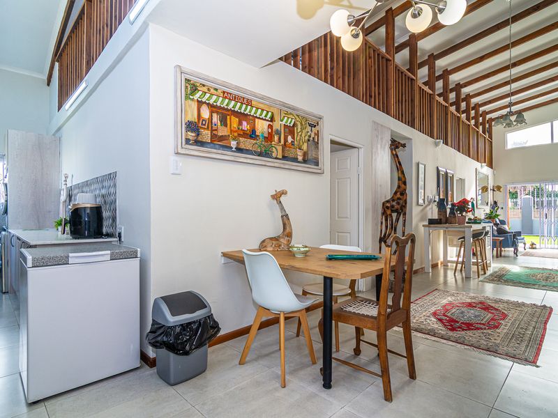 Spacious open-plan living area featuring high ceilings with exposed timber beams, a mezzanine level, and a functional kitchen space with tiled flooring.