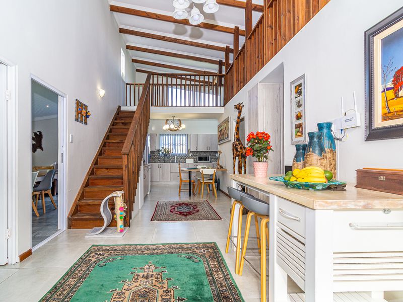 Spacious open-plan living area featuring exposed timber ceiling beams, a wooden staircase leading to a mezzanine level, and a functional kitchen with tiled flooring.