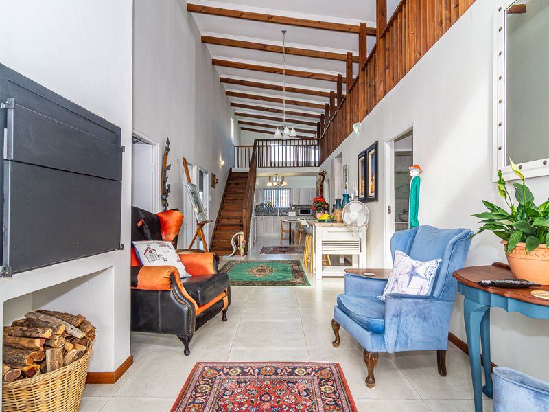 Spacious open-plan living area featuring exposed timber ceiling beams, a built-in fireplace, and a staircase leading to a mezzanine level.