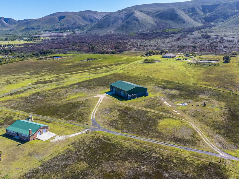 Aerial view of a farm property featuring a main farmhouse, a large metal shed, and expansive surrounding grazing land with mountain views.