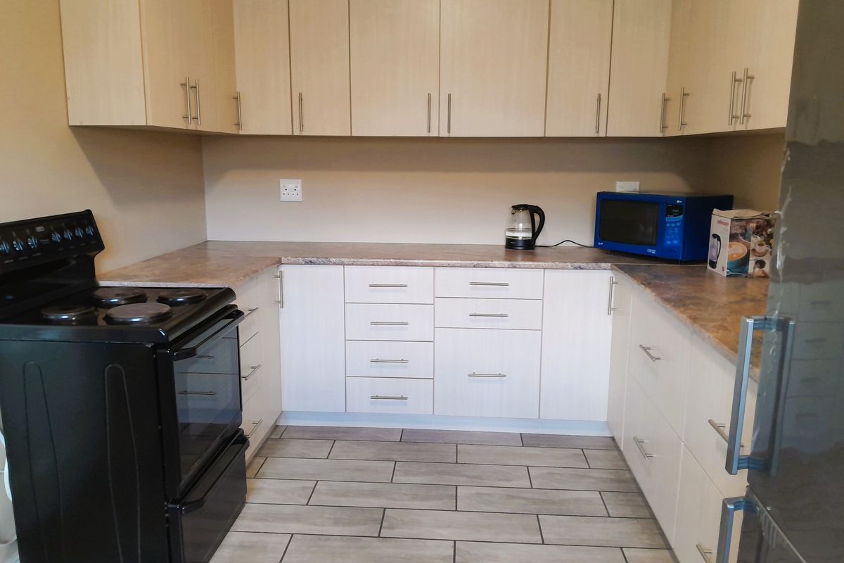 A functional kitchen featuring light-toned laminate cabinetry, stone-look laminate countertops, and modern ceramic tile flooring, providing a clean and practical workspace.