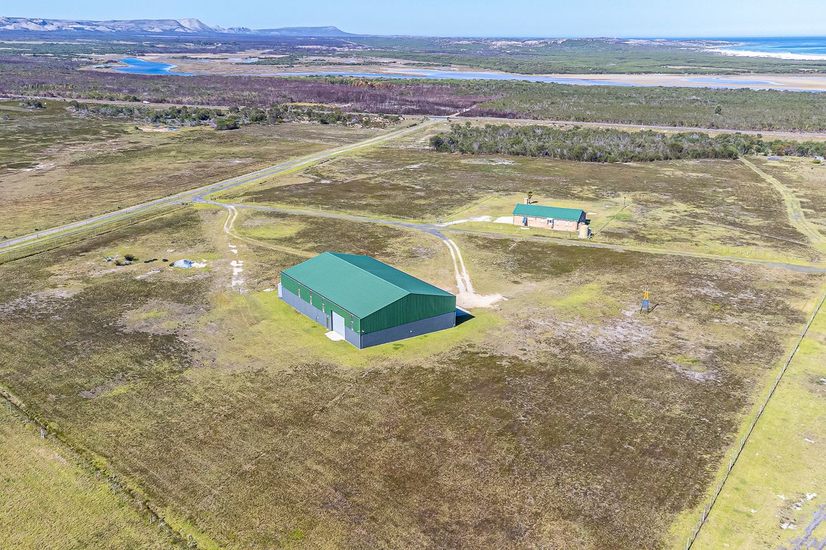 Aerial view of a large farm property featuring a substantial metal shed, a secondary dwelling, and expansive open land with coastal landscape views.