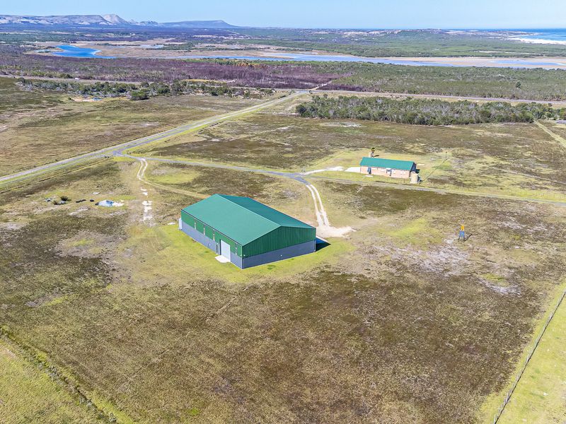 Aerial view of a large farm property featuring a substantial metal shed, a secondary dwelling, and expansive open land with coastal landscape views.