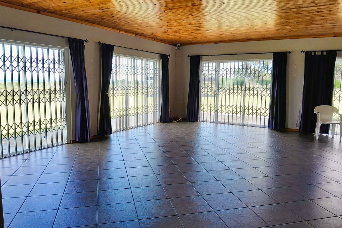 Spacious living area featuring tiled flooring, a warm timber ceiling, and multiple sliding glass doors with security gates providing access to the garden.