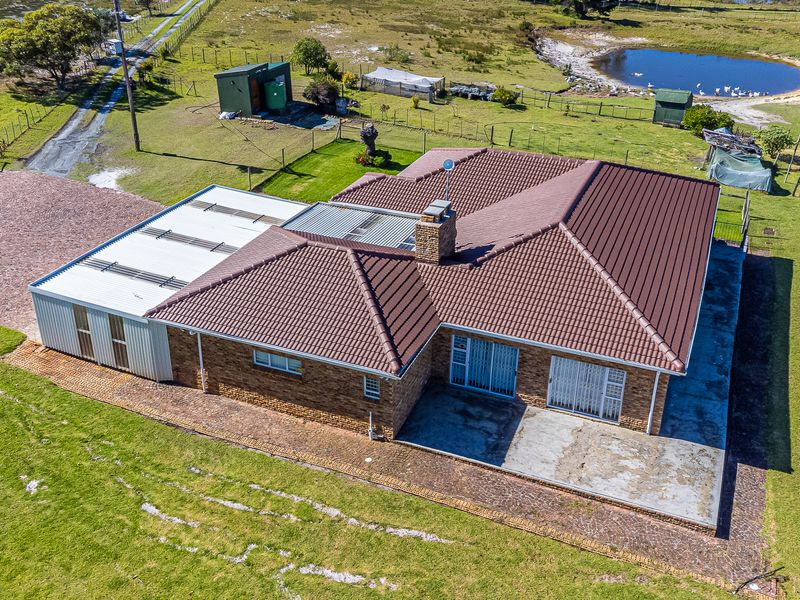 Aerial view of a brick farmhouse featuring a tiled roof, attached metal garage, and a concrete patio set within a rural landscape.
