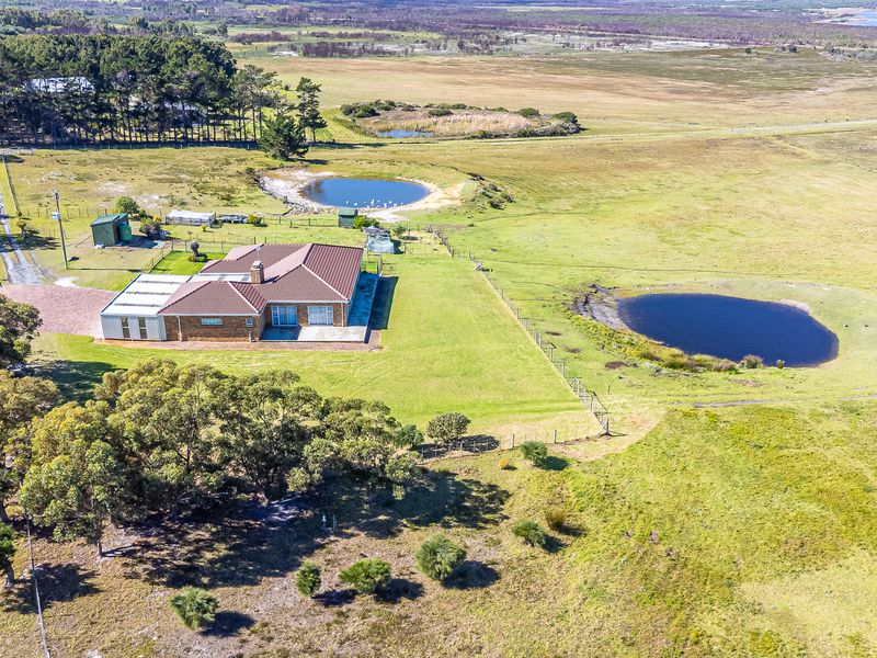 Aerial view of a farm property featuring a brick residence with a metal roof, surrounded by open pasture, mature trees, and two farm dams.